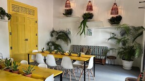 A modern interior with a yellow door, white chairs, a wooden dining table, and hanging red pendant lights.