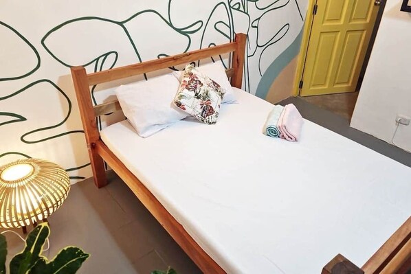 A neatly made bed with a wooden frame, white bedding, and a floral pillow.