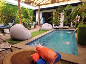 A pool area with a hot tub, two bean bags, and a hammock.
