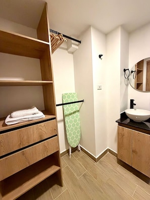 A bathroom with wooden shelving, a green ironing board, a sink, and a mirror. - 81 Living (Medellín)