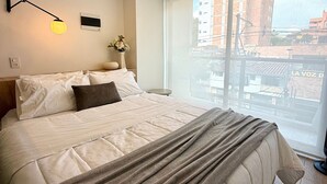 Hotelkamer met een groot bed, een nachtkastje, een wandlamp en een raam met uitzicht op de stad.