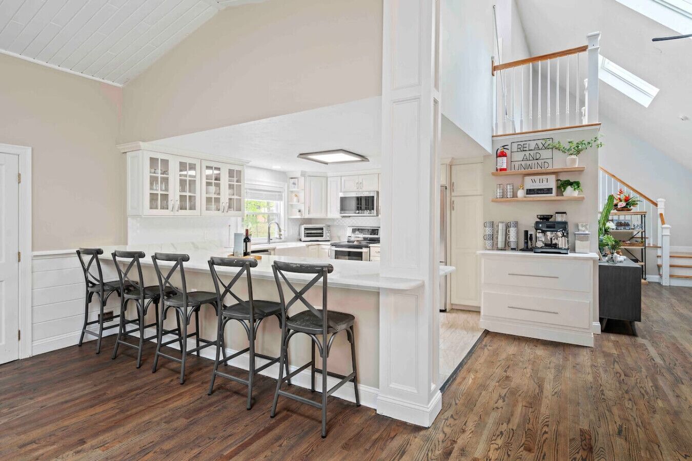 Una cocina amplia con armarios blancos, una isla central con taburetes y suelo de madera.
