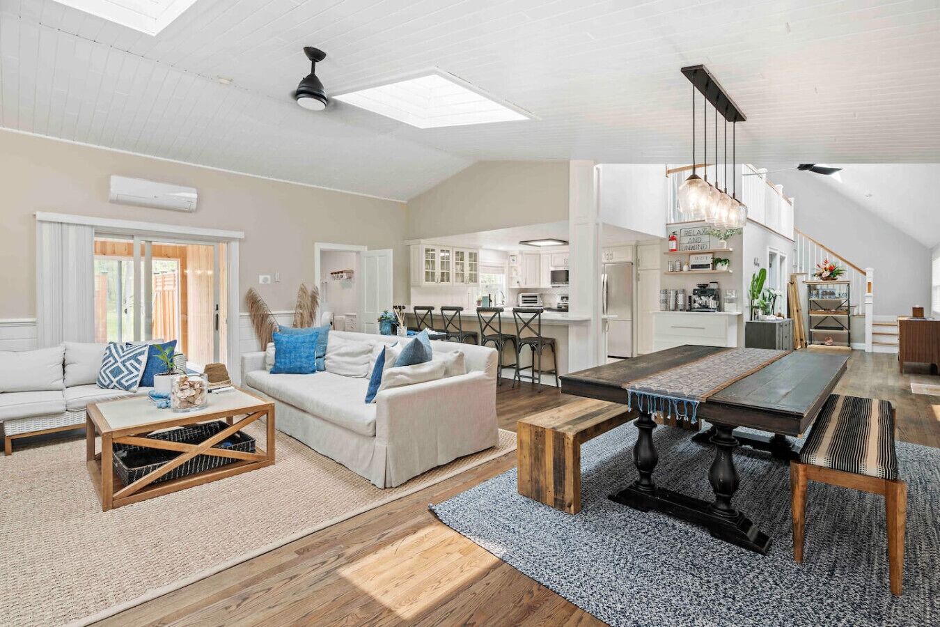 Ein großzügiger Wohnbereich mit einer Couch, einem Couchtisch und einem Esstisch. Im Hintergrund befindet sich eine Küche mit weißen Schränken und ein Essbereich mit Stühlen.