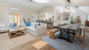 A spacious living area with a sofa, coffee table, and dining table. There is a kitchen in the background with white cabinets and a dining area with chairs.