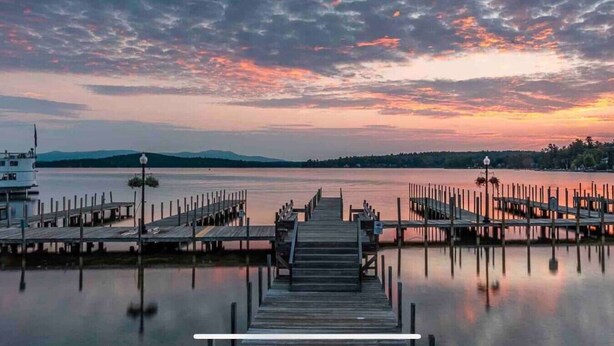 A wooden pier extending into calm water with a boat docked on the left and a row of street lamps along the pier.