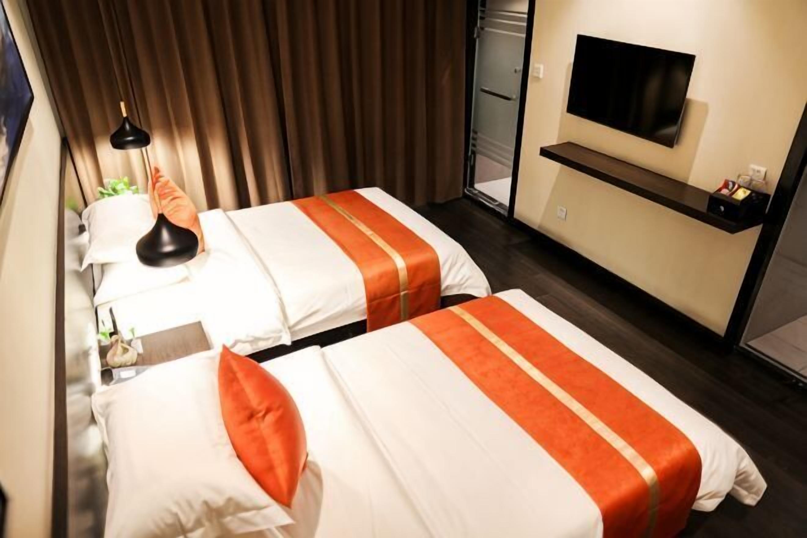 A hotel room with two beds, a TV, a desk, and a window with curtains.