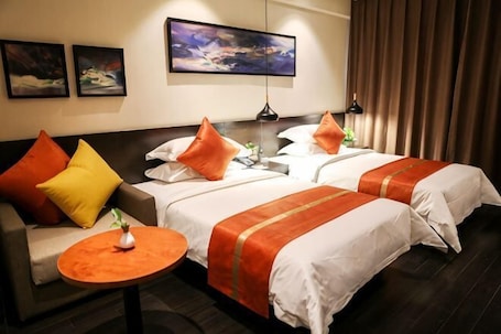A hotel room with two beds, a sofa, a small round table, and a painting on the wall.. Boru Hotel