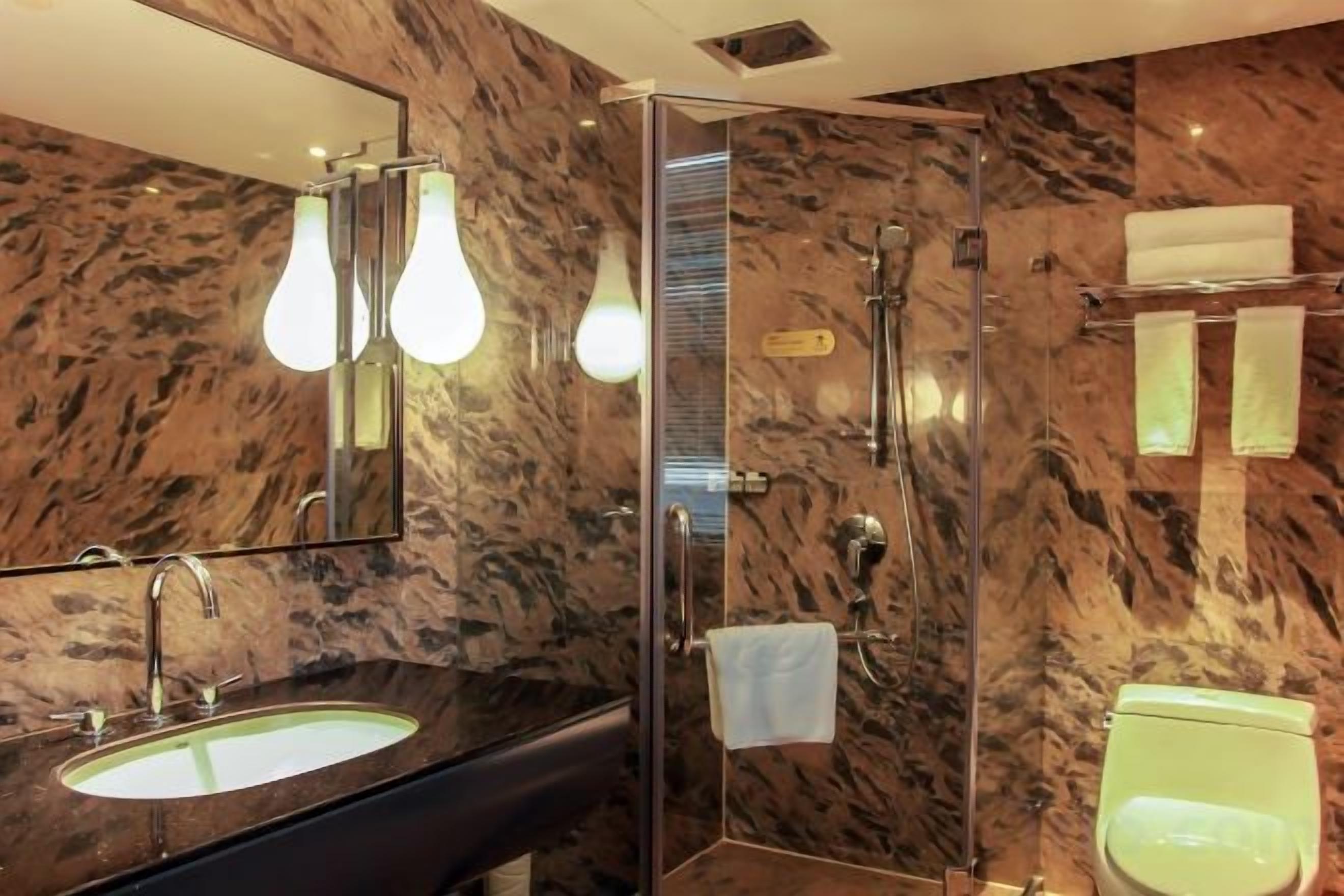 Un baño con pared de mármol, lavabo, espejo y ducha.