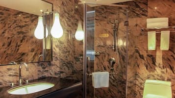 Un baño con pared de mármol, lavabo, espejo y ducha.