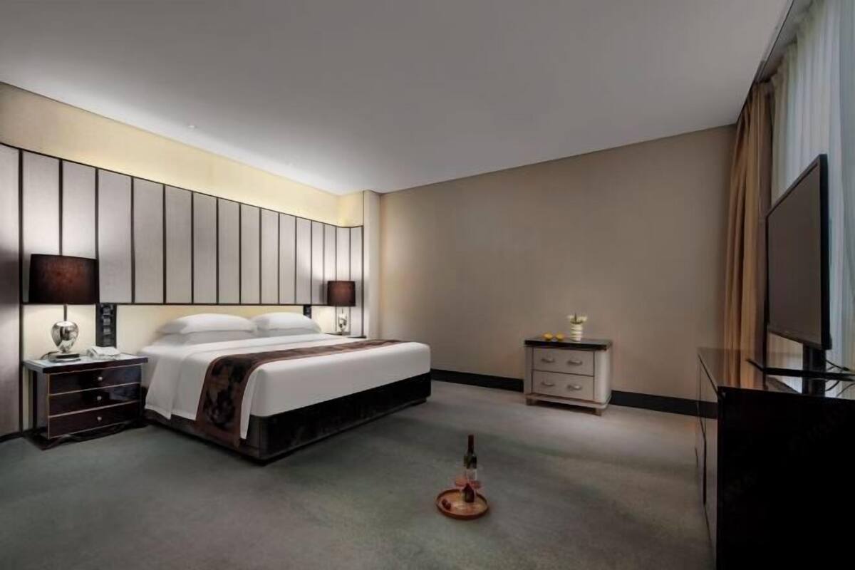 A hotel room with a large bed, bedside tables, a TV, and a minibar.