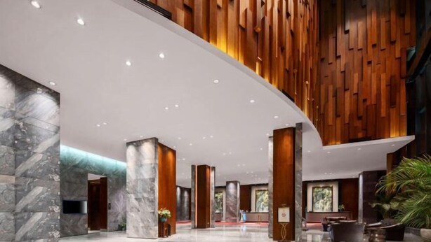 Un vestíbulo amplio con techo curvo, columnas de mármol, paneles de madera y un mostrador de recepción.