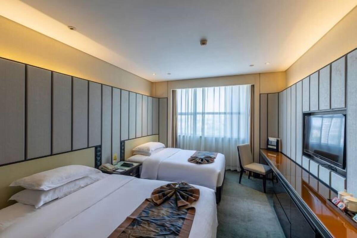 A hotel room with two beds, a desk, a chair, a TV, and a large window.