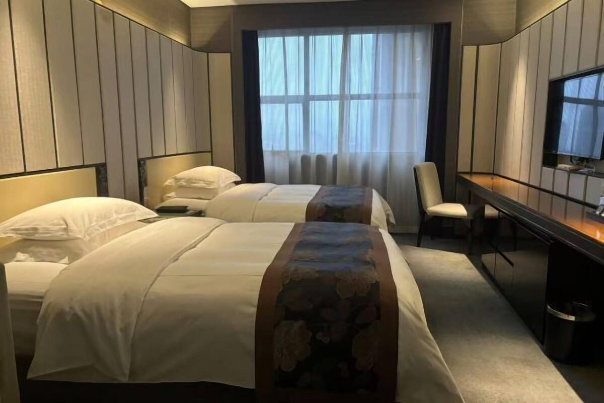 A hotel room with two beds, a desk, a chair, a television, and a window with curtains.