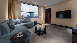 Una sala de estar moderna con un sofá, una mesa de centro redonda de vidrio, un televisor de pantalla plana y un ventanal con vista a la ciudad.