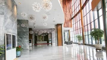 Un vestíbulo amplio con piso de mármol pulido, una mesa de recepción y ventanas grandes.