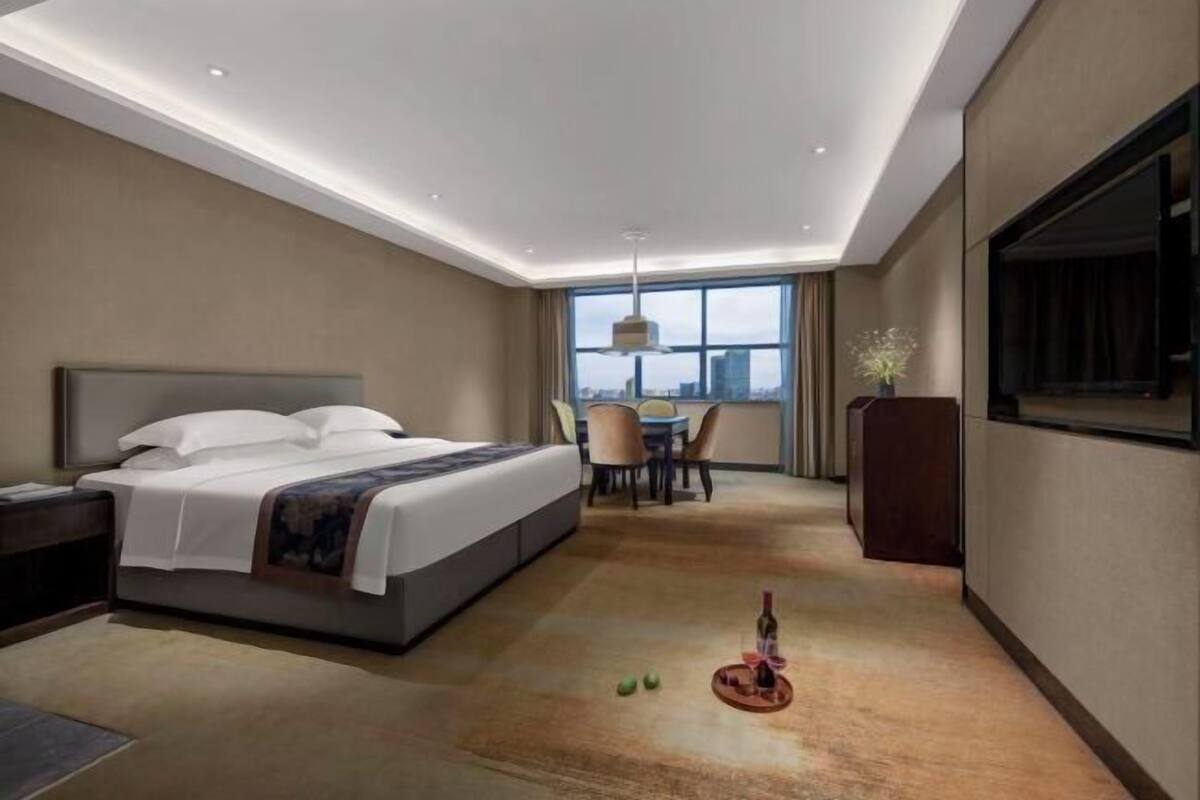 A hotel room with a bed, a dining table, chairs, a TV, and a city view.