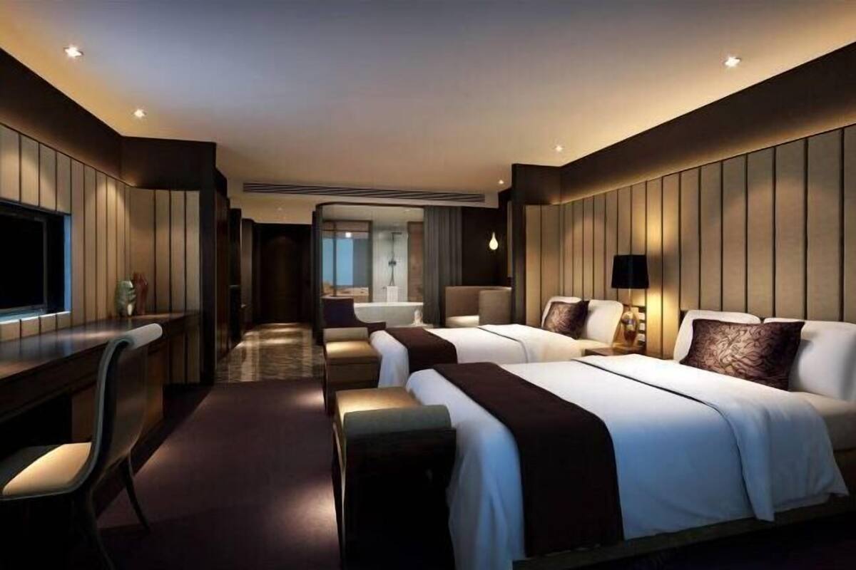 A hotel room with two beds, a desk, a chair, and a TV.