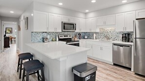 A modern kitchen with white cabinets, a central island, stainless steel appliances, and a patterned backsplash. - Charming 2-bedroom condo with WiFi, AC in lovely Destin (Destin)