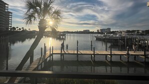 A marina with boats docked, a wooden pier, and a palm tree silhouetted against the sky. - Charming 2-bedroom condo with WiFi, AC in lovely Destin (Destin)