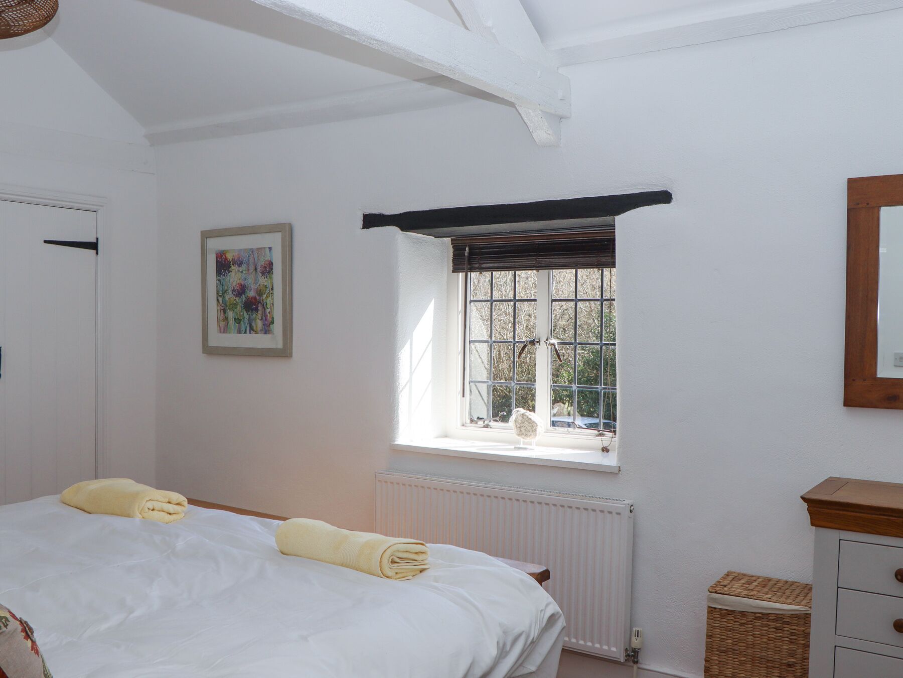 A bedroom with a bed, a window with a view, a radiator, and a wooden dresser.