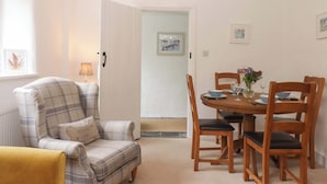 A dining area with a table set for four, a plaid armchair, a yellow armchair, and a wooden dining table with chairs. - 2 New Mill Cottages (Newton Abbot)