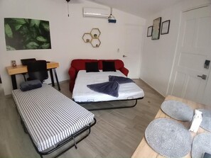 Une chambre avec deux lits simples, un bureau avec une chaise, un canapé rouge, une table en bois avec une chaise et un climatiseur fixé au mur.
