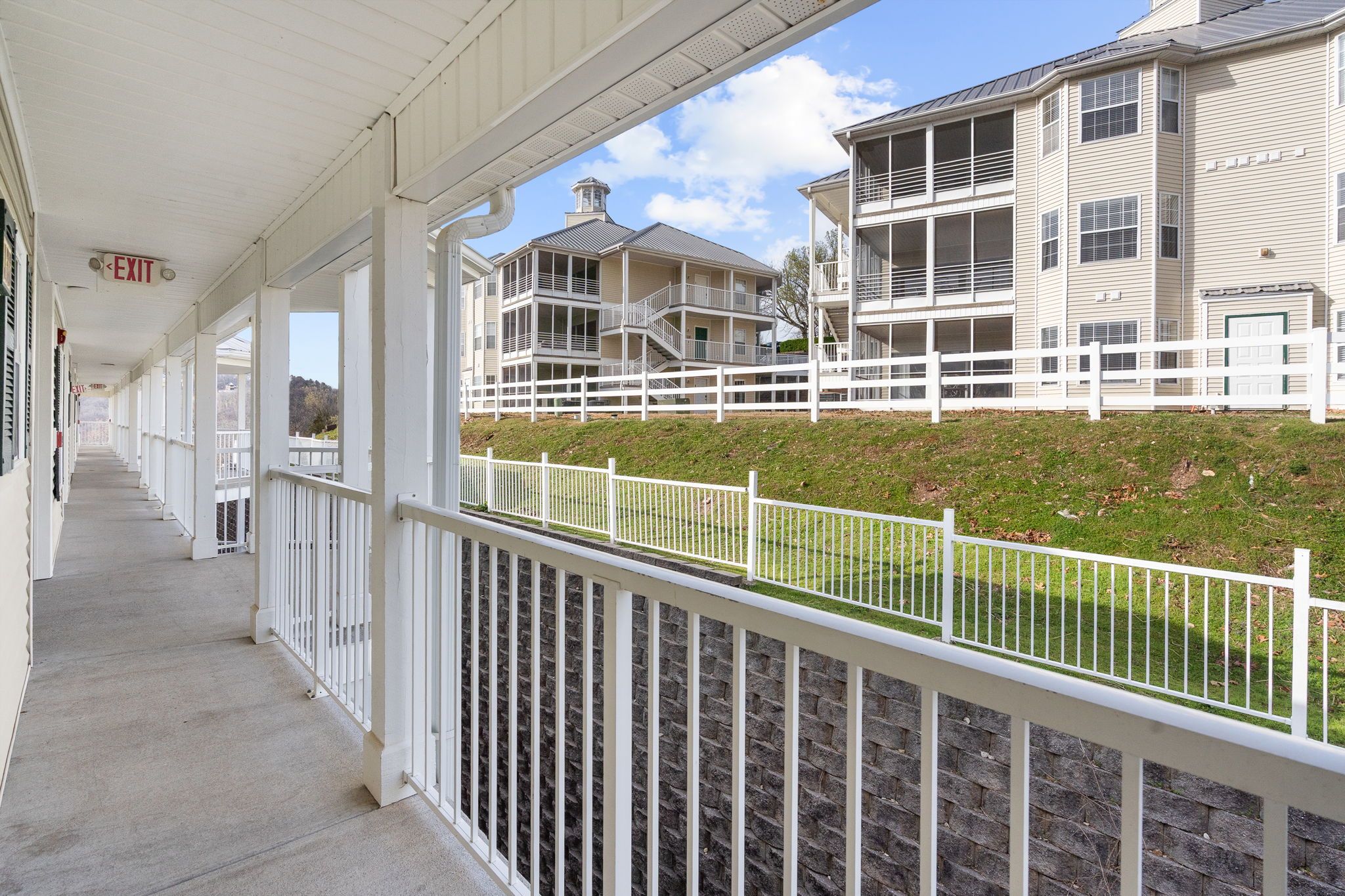 A covered walkway with a white railing, leading to a building with multiple balconies and a white fence.