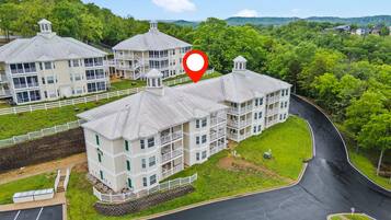 A multi-story building with balconies, a parking lot, and a surrounding green landscape.