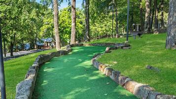 A green artificial turf golf course with stone borders and trees in the background.