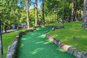 A green artificial turf golf course with stone borders and trees in the background.