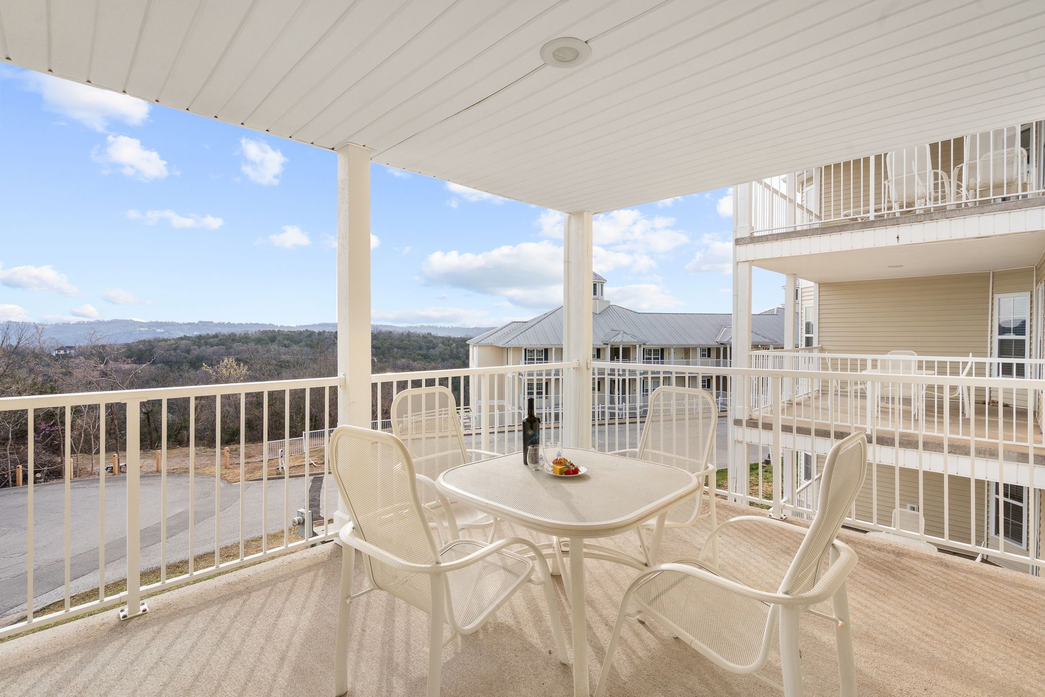 A balcony with a table and chairs, overlooking a road and buildings.
