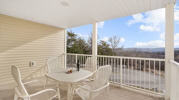 A covered balcony with a table and chairs, overlooking a parking area and distant landscape.