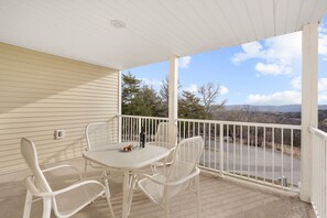 A covered balcony with a table and chairs, overlooking a parking area and distant landscape.