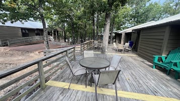 Une terrasse en bois avec un espace salon extérieur, comprenant une table et des chaises, entourée d’arbres.