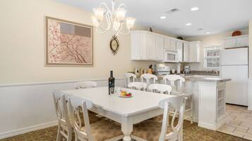 A kitchen with white cabinets, a white dining table, and chairs. There is a clock on the wall and a chandelier above the table.