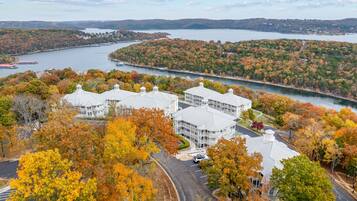 A large building with multiple wings, surrounded by autumn foliage and a body of water.