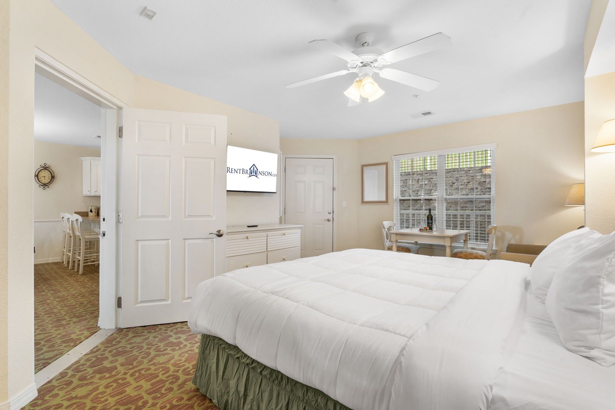 A hotel room with a bed, a desk, a chair, a ceiling fan, and a television.