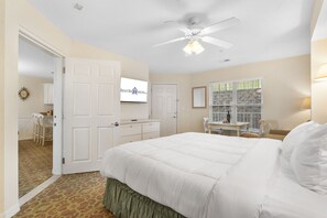 Una habitación de hotel con una cama, un escritorio, una silla, un ventilador de techo y un televisor.