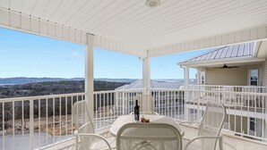 Un balcón cubierto con sillas y una mesa de metal blanco, con vistas a un paisaje pintoresco.