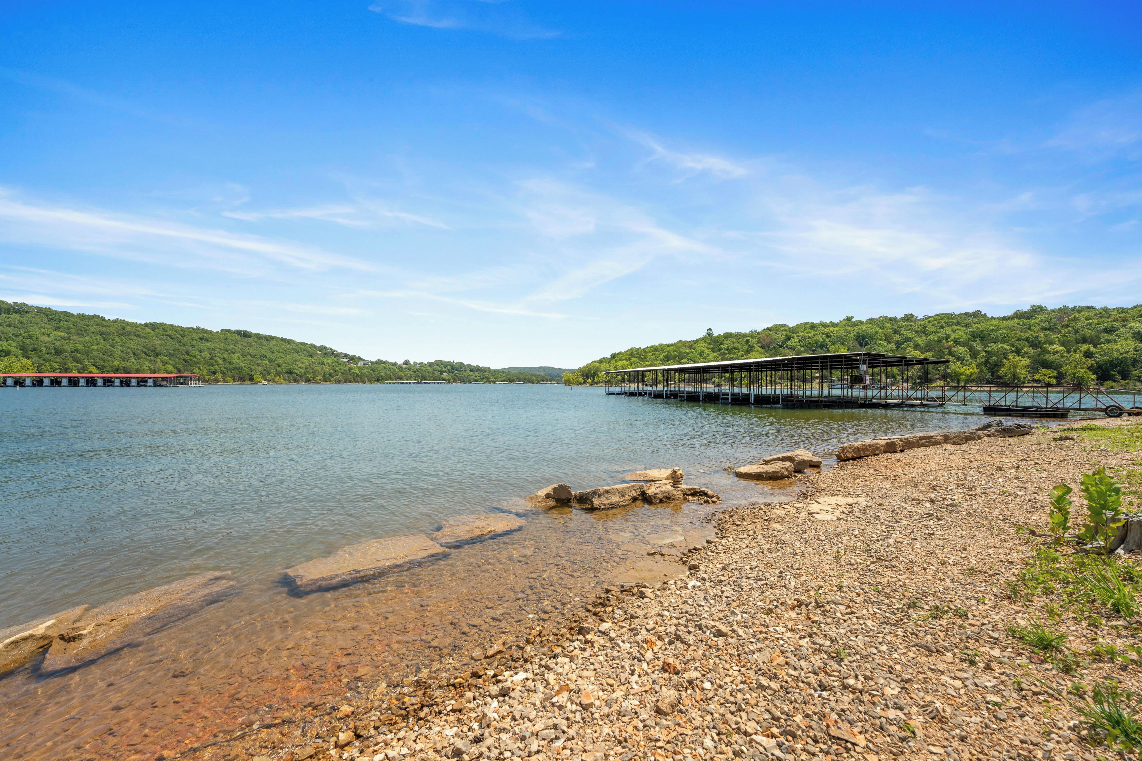 A lakeside view with a dock extending into the water, surrounded by rocky terrain and lush greenery.