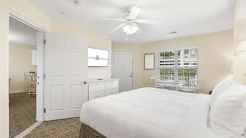 A bedroom with a bed, a ceiling fan, a desk, and a window with blinds.