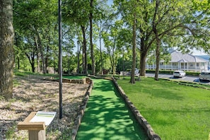 A golf course with a green path, trees, and a building in the background.