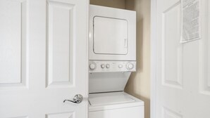 A laundry room with a stacked washer and dryer, a door with a key lock, and a wall-mounted paper dispenser. - Table Rock Lake-Access Kim City Condo w/ Community Pool, Mini Golf & Free Daily Tickets (Kimberling City)