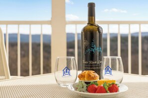 Eine Weinflasche, zwei Gläser und ein Teller mit Erdbeeren und Gebäck auf einem Balkon mit Bergblick.