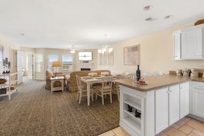A spacious living area with a dining table, sofas, and a kitchen with white cabinetry.
