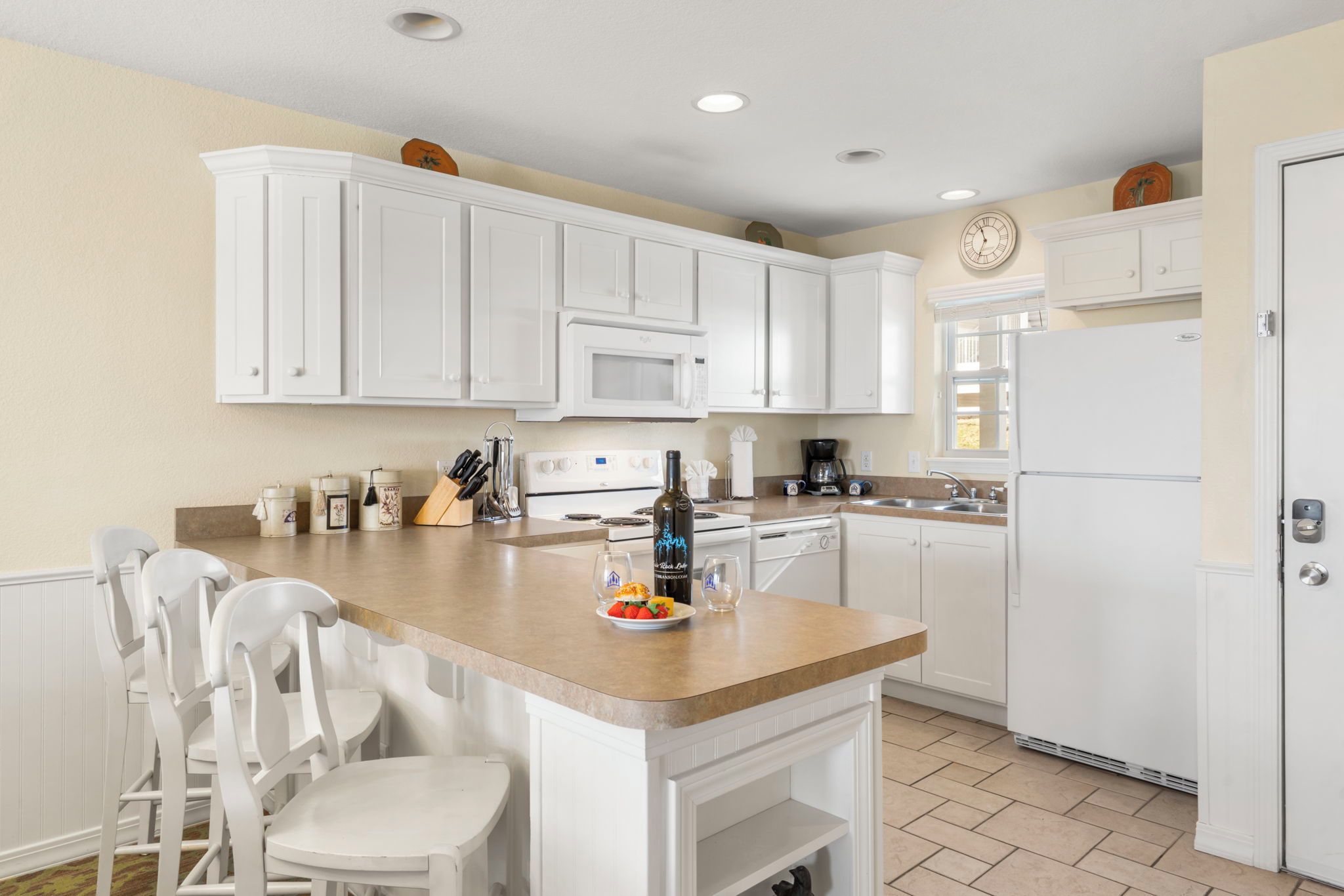 A kitchen with white cabinets, a central island with chairs, a microwave, a stove, and a refrigerator.