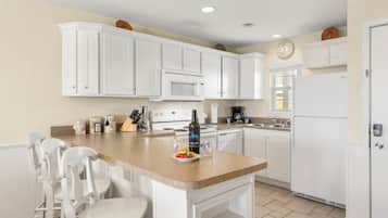 A kitchen with white cabinets, a central island with chairs, a microwave, a stove, and a refrigerator.