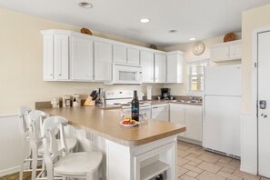 A kitchen with white cabinets, a central island with chairs, a microwave, a stove, and a refrigerator.