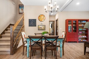 Un coin repas avec une table et des chaises en bois, un escalier et un meuble rouge contenant des jeux.