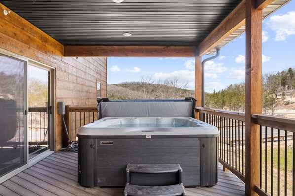 A hot tub on a wooden deck with a glass door leading to a covered area.